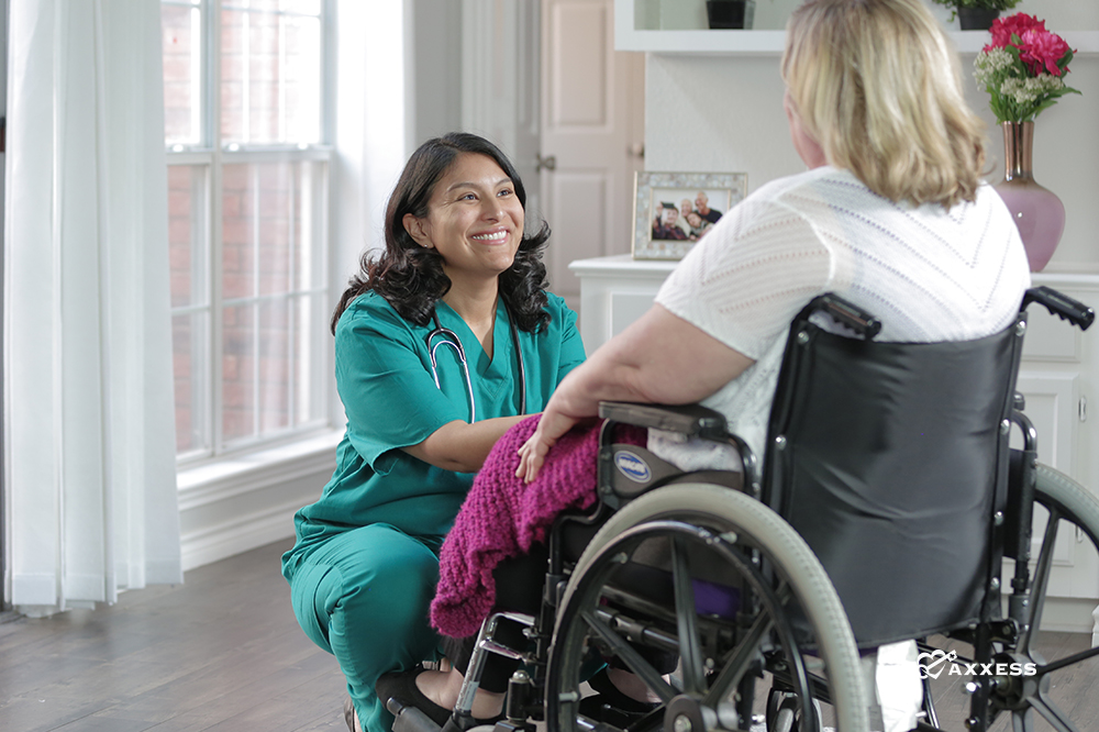 A nurse kneeling in front of a patient sitting a wheelchair.