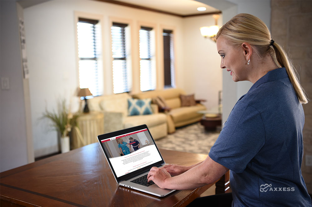 Clinician sitting at a table while viewing the Axxess PDGM resource page on her laptop