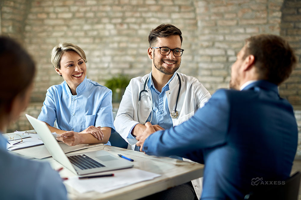 Clinicians sit together at a table and shake hands on a business deal.