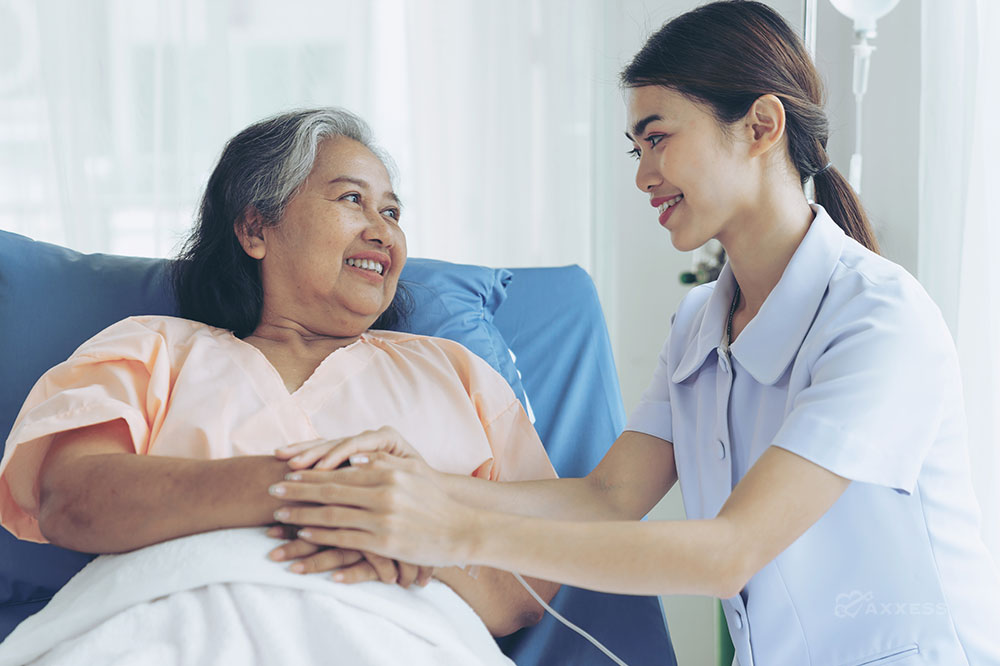 An elderly female patient in bed looks fondly at a young female clinician