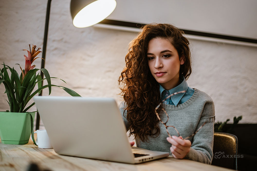 Brunette woman holding glasses sits in front of a laptop