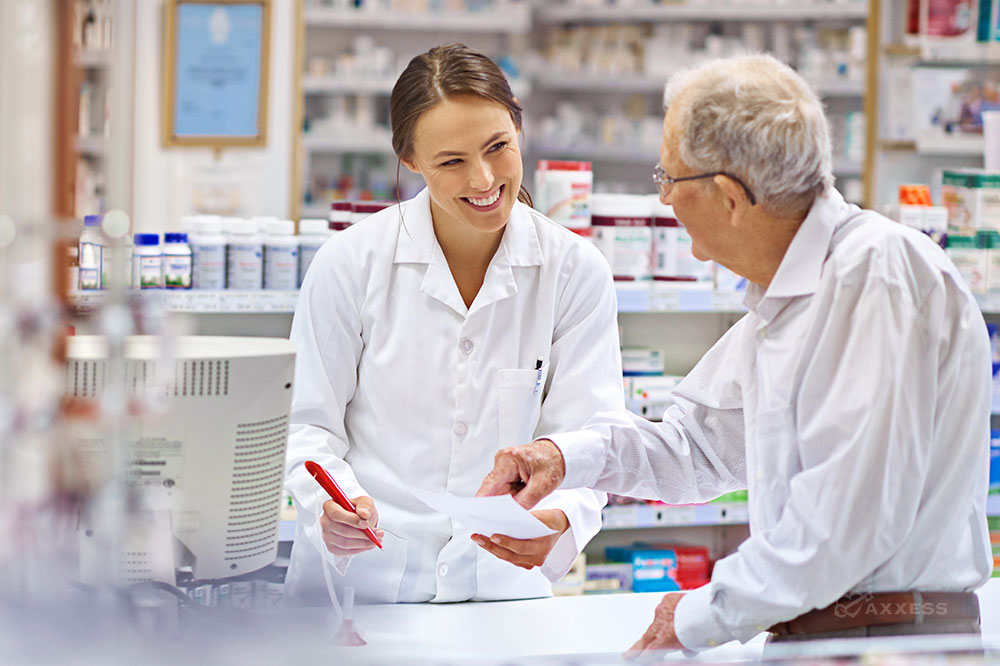 A pharmacist and elderly man speak at a pharmacy counter