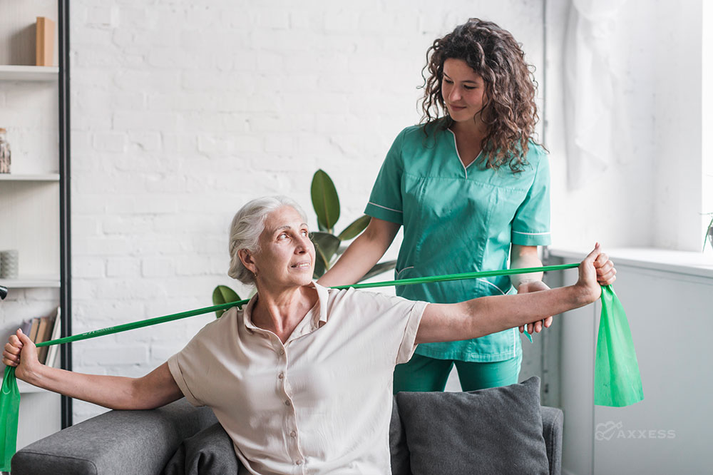 A physical therapist assist a seated older client with a stretch band.