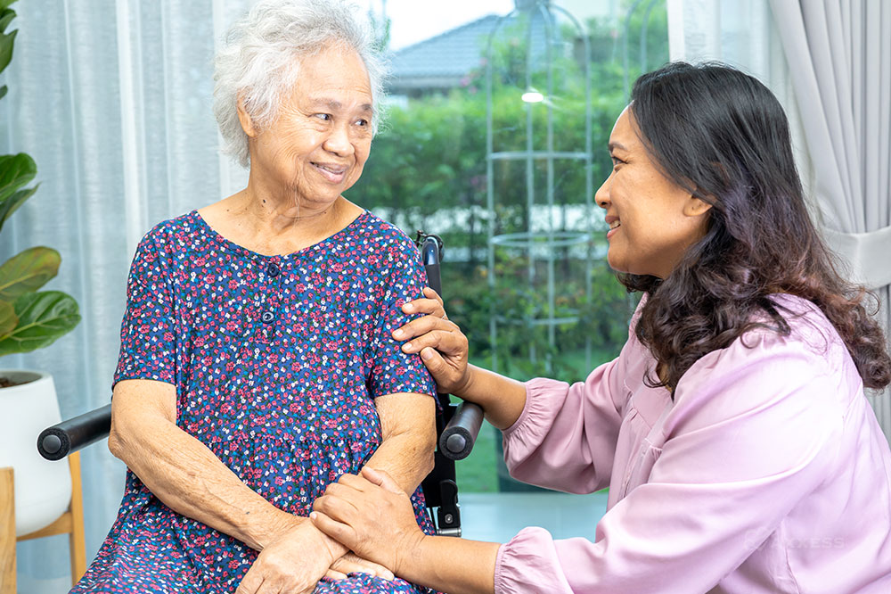 Member of hospice IDG kneels next to elderly woman in wheelchair