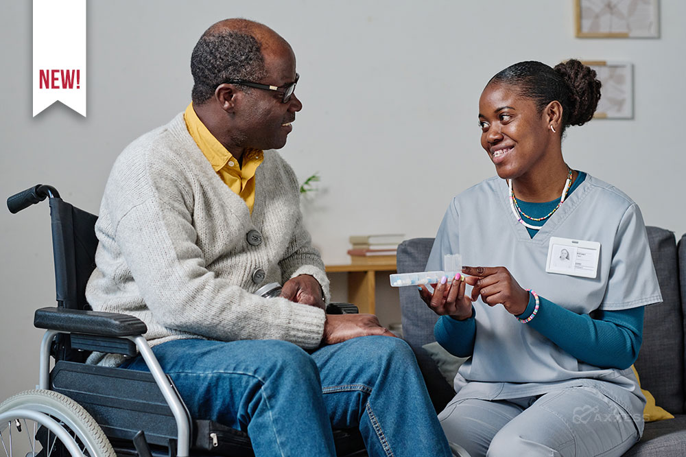 A female clinician smiles while sitting next to an elderly man in a wheelchair