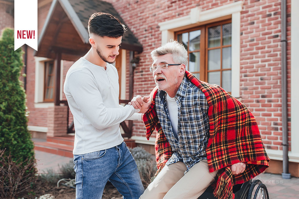 A young adult male assists an elderly man getting up from his wheelchair.