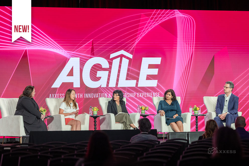 A panel of five people sit on stage at a conference. The background is a large pink screen with the word "Agile" in white letters. The word "New" is in a white banner in the upper left corner. The Axess logo is in the lower right corner.