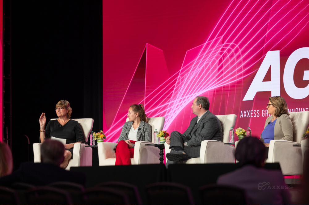 Four people are sitting on a stage having a conversation. There is a large screen behind them that says AGILE.