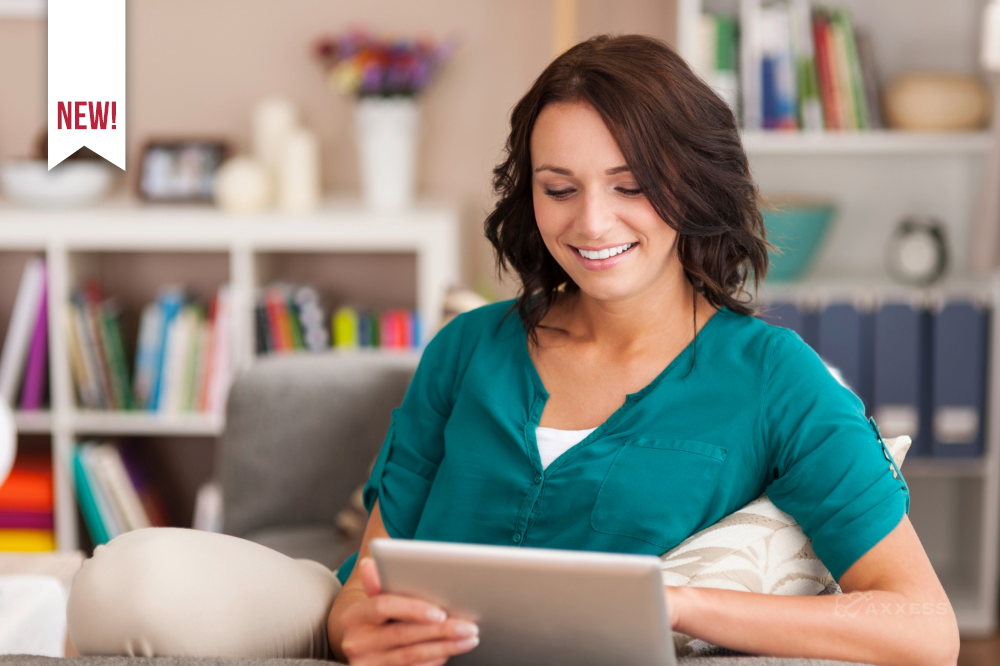 Person sitting on a couch in a cozy living room, holding a tablet and looking at the screen, with a bookshelf and decorative items in the background.