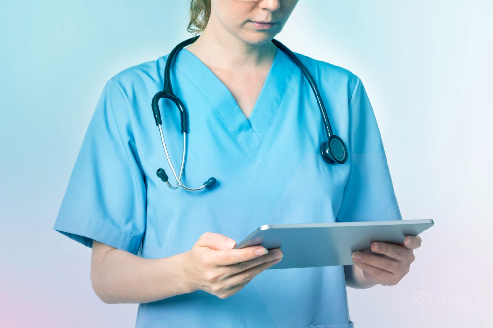 A healthcare professional in light blue scrubs with a stethoscope around their neck holds a tablet and reviews information on the screen. The softly lit background features blue and pink gradient tones, emphasizing a modern, technology‑enabled care setting.